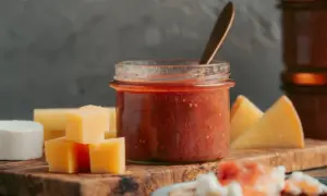Glas mit rotem Chutney, daneben Käsewürfel und -stücke. Perfekt für leckere Chutneys Rezepte.