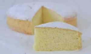 Una soffice torta con farina di riso, spolverata di zucchero a velo, con una fetta tagliata.