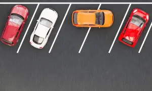 Cztery samochodziki na parkingu, gotowe do równoległego parkowania. Czerwony, biały, pomarańczowy i znów czerwony.