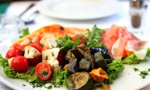 Assiette d'antipasti colorée : tomates cerises, mozzarella, légumes grillés, jambon cru et une part de pizza. Une recette d'antipasti parfaite pour l'été.
