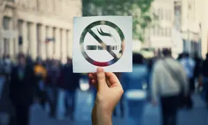Dłoń trzyma kartkę z symbolem zakazu palenia na tle miejskiego tłumu.