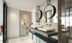 Un moderno baño con dos lavabos sobre encimera de piedra, espejos circulares colgantes y armarios integrados. Se puede hacer un baño en una habitación así.