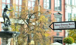 Fontanna Neptuna i drogowskaz na Ratusz Głównego Miasta w altstadt Danzig. Jesienne liście drzew tworzą tło dla zabytkowej architektury.