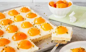 Ciasto z brzoskwiniami, przypominające jajko sadzone, posypane pistacjami. Na blasze i talerzyku.