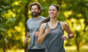 Coppia sorridente corre nel parco. Lei, in primo piano, è determinata, lui la segue con gioia. Un esempio di come iniziare a correre a 50 anni sia possibile e appagante.