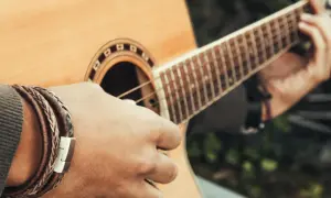 Dłoń z bransoletką z plecionej skóry gra na cdur gitarze.