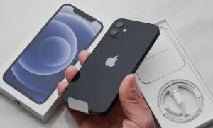 Czarny iPhone w ręce, obok pudełko z telefonem i kablem.