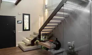 Modernas escaleras interiores prefabricadas con peldaños flotantes de hormigón y barandilla de cristal. Una cascada interior ilumina el espacio.
