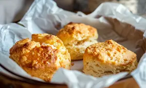 Tre gyllene, lätta scones ligger i ett papper. Perfekta för en fika.