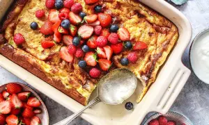 En gyllene ungspankaka toppad med färska jordgubbar, hallon och blåbär. Serveras med en skål bär och gräddfil.