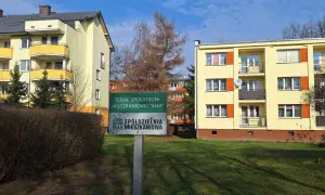 Zielony znak z napisem "TEREN SPÓŁDZIELNI MIESZKANIOWEJ 'IHAR'" przed żółtymi blokami mieszkalnymi.