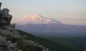 Majestatyczne gory z elbrusem w różowym świetle zachodzącego słońca. Na pierwszym planie skaliste zbocze.