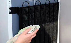 Ręka czyści czarny skraplacz w lodówce. Dbanie o niego zapewnia jej sprawne działanie.