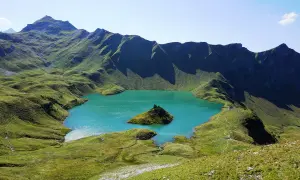 Türkiser Bergsee in Deutschland mit einer kleinen Insel, umgeben von grünen, schattigen Berghängen.