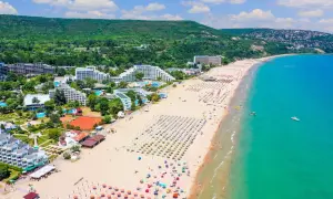 Słoneczna plaża w Bułgarii, pełna leżaków i parasoli, z turkusowym morzem i zielonymi wzgórzami w tle.