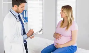 Położnik w białym kitlu notuje coś na kartce, rozmawiając z uśmiechniętą ciężarną.