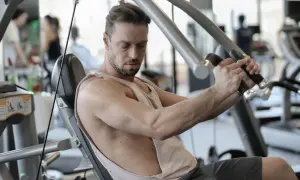 Mann trainiert im Fitnessstudio, um schnell zuzunehmen. Er sitzt auf einem Gerät und drückt die Griffe nach vorne.