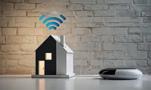 Model domu z zapalonymi oknami i drzwiami, nad którym unosi się symbol wi-fi. Obok stoi nowoczesny router.