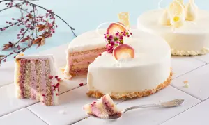 Delikatne torty z różowym kremem i owocami. Widoczne jakie warstwy do tortu, ozdobione białymi czekoladowymi figurkami i kwiatami.