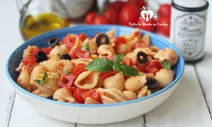 Un piatto di pasta con ricotta e pomodorini freschi, arricchito da olive nere e basilico.