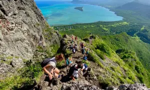 Wanderer erklimmen den Le Morne Brabant, eine atemberaubende Bergformation mit Blick auf das türkisfarbene Meer und üppige grüne Landschaften.