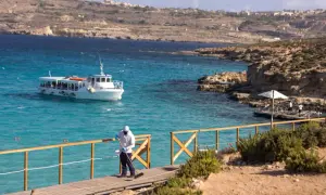 Malta, lipiec: słoneczna pogoda zachęca do rejsu statkiem po turkusowej wodzie. Pracownik sprząta drewniany pomost.