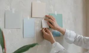 Händer arrangerar färgglada papper på en vägg. Tre tavlor bredvid varandra bildar en del av en moodboard.