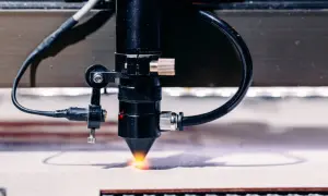 Precyzyjne cięcie sklejki laserem. Widoczny detal głowicy tnącej z wiązką światła.
