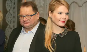 Mężczyzna w okularach i jego żona, ubrana w czarną sukienkę z ozdobnym kołnierzykiem, pozują do zdjęcia.