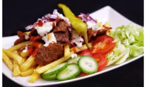 En tallrik med kebab, pommes frites, tomater, gurka, sallad och en grön chili. Perfekt för dig som söker ett gott kebabsås recept.