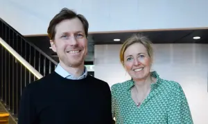 Tobias Sahlin ler glatt bredvid en kvinna i grön mönstrad blus. De står framför en trappa med belysning.