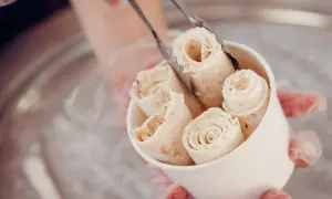 Rolowane lody cassate w kubeczku, przygotowywane przez ręce w rękawiczkach.