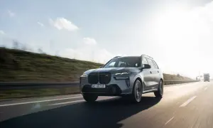 Szary BMW X7 M60i pędzi autostradą w słoneczny dzień.
