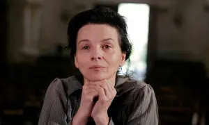 Portret kobiety w wieku dojrzałym, przypominającej Camille Claudel, z dłońmi podpartymi pod brodą, w stonowanym wnętrzu.