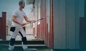 Man målar om huset med en lång roller. Den röda träfasaden får nya grå paneler.