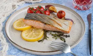 Gebratener Lachs mit Haut, serviert mit Zitronenscheiben, Kirschtomaten und Kräutern. Ein köstliches Rezept für Lachs mit Haut.