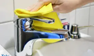 Hand poliert glänzenden Wasserhahn mit gelbem Tuch. Der Wasserhahn geht schwer, aber die Reinigung macht ihn wieder leichtgängig.