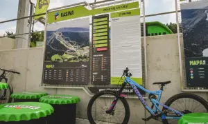Mapa tras w bike parku Kasina z regulaminem i oznaczeniami trudności. Obok stoi rower enduro.