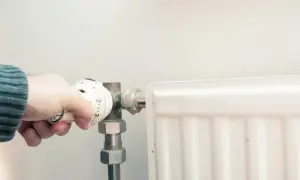 Dłoń reguluje termostat, próbując poradzić sobie z zapowietrzonym kaloryferem w bloku.