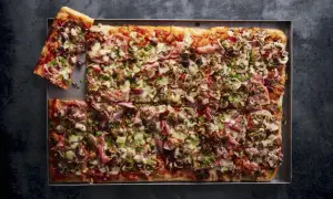 Pyszna pizza domowa przepis na blachę z szynką, pieczarkami i oliwkami, posypana serem i natką pietruszki.