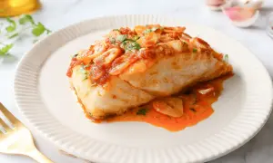 Delicioso bacalao a la llauna con salsa de tomate y ajo, servido en un plato blanco con un tenedor dorado.