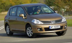 Złoty Nissan Tiida z mężczyzną za kierownicą jedzie po drodze.