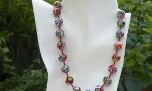 Colgantes de cristal de Murano, un collar vibrante con cuentas esféricas multicolores, cada una con un diseño floral único, sobre un fondo verde exuberante.