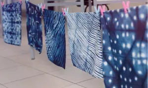 Stoffbahnen mit verschiedenen blauen Batik-Techniken trocknen an einer Leine. Muster wie Wellen, Punkte und abstrakte Formen sind sichtbar.