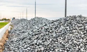 Duże hałdy kruszywa, idealnego jako żwir do betonu, czekają na budowie. W tle widać latarnie i niebo.
