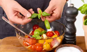 Hände geben Basilikumblätter in eine Schüssel mit Tomaten und Zwiebeln.