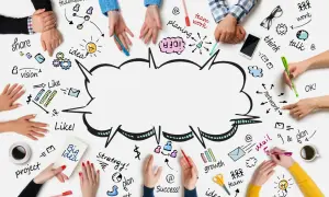 Ludzie tworzą burzę mózgów, rysując na stole słowa: teamwork, idea, plan, vision, share, think, talk, growth, success.