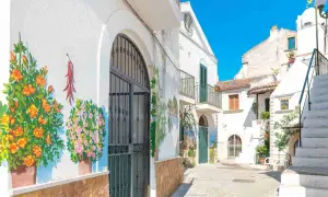 Vicolo fiorito nel centro storico di Rodi Garganico, con murales colorati su muri bianchi e un cielo azzurro brillante.