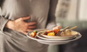 Osoba trzyma stos brudnych talerzy, czując uczucie pełności w żołądku po obfitym posiłku.