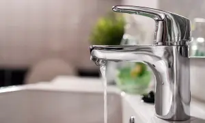 Chromowany kran jednouchwytowy z cieknącą wodą nad białą umywalką.